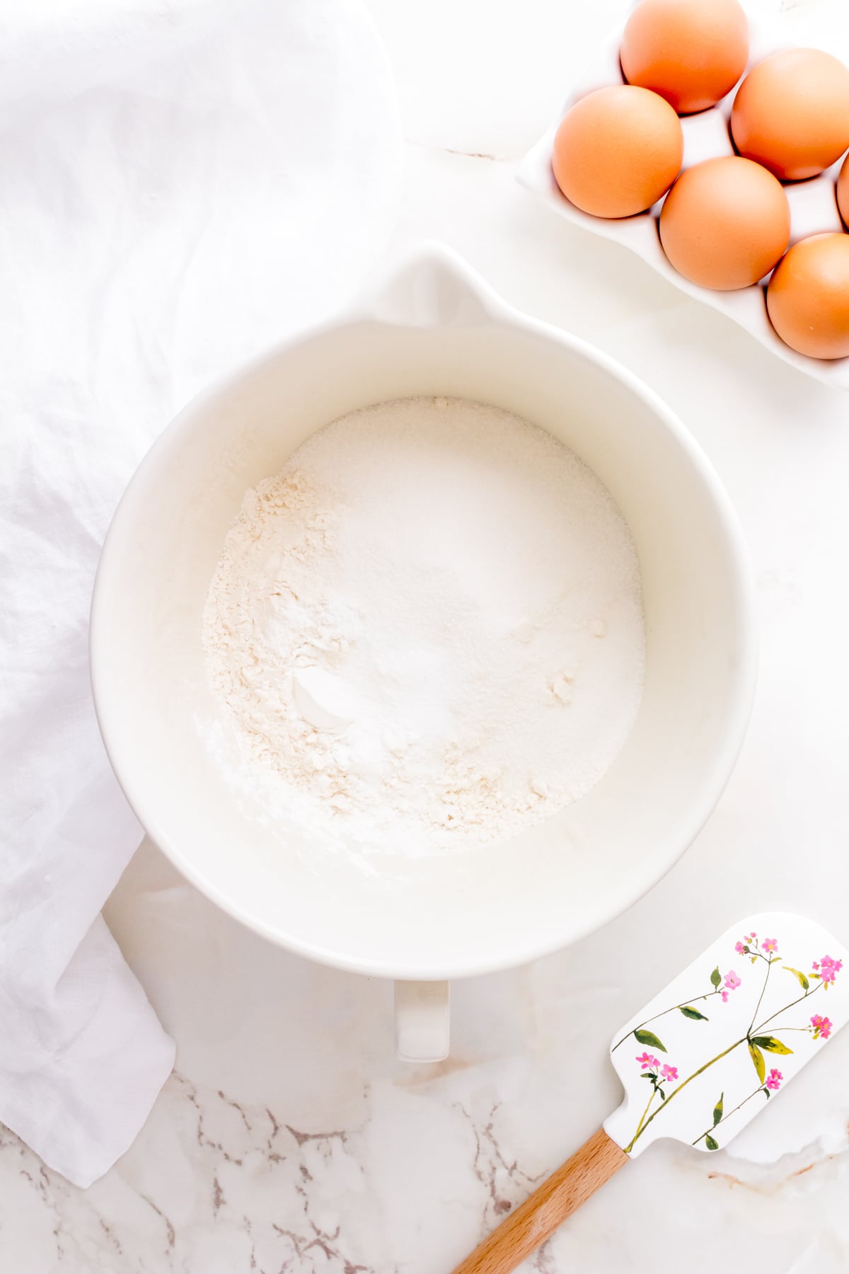 flour, sugar, baking powder, cornstarch and salt whisked together in a white bowl for buttermilk waffle batter.
