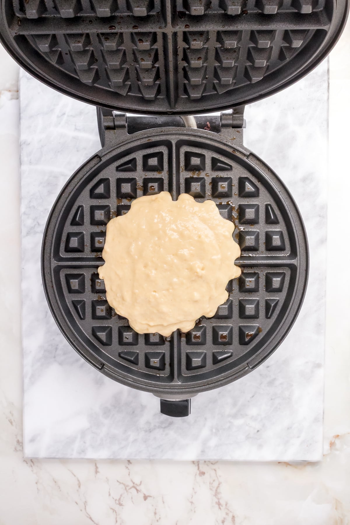 Buttermilk waffle batter being on a hot Belgian waffle iron.
