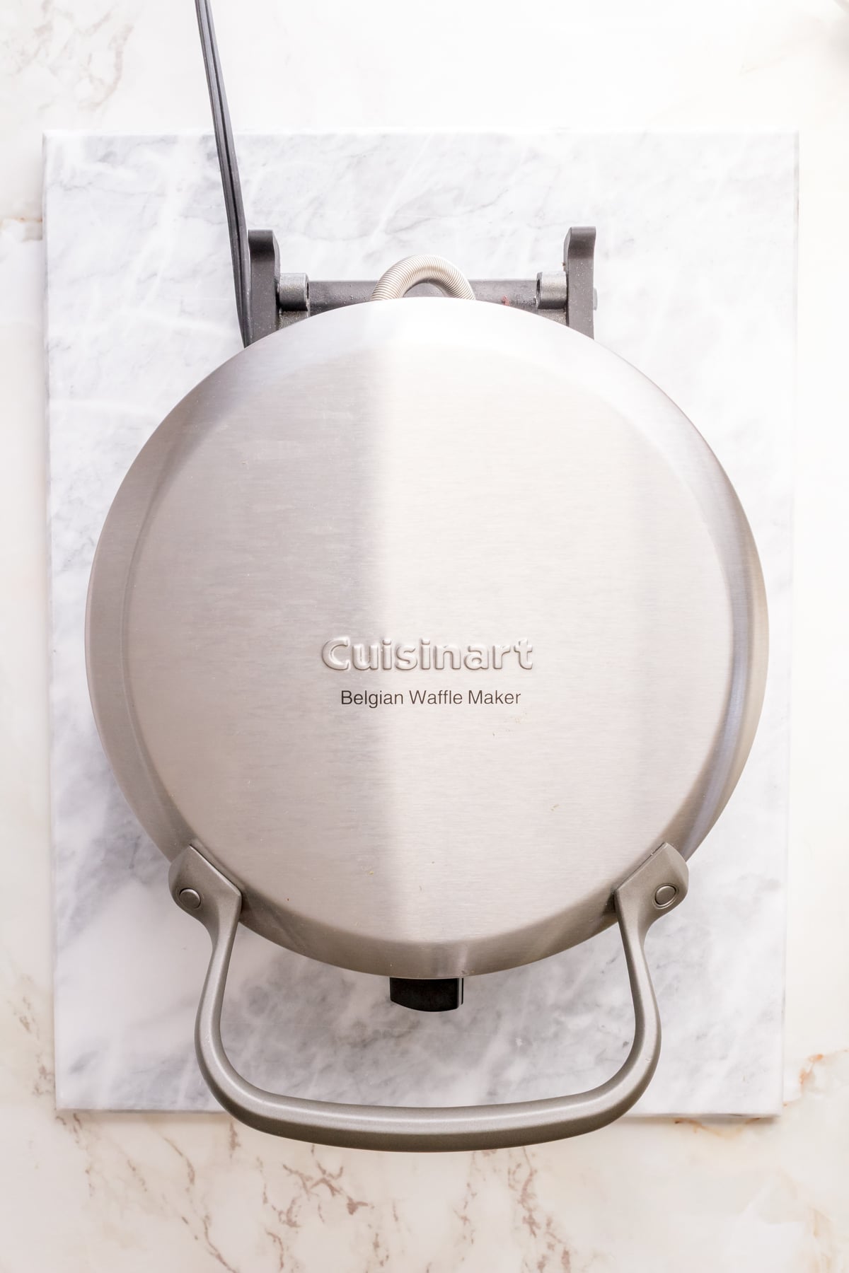 Belgian waffle iron preheating on marble counter.