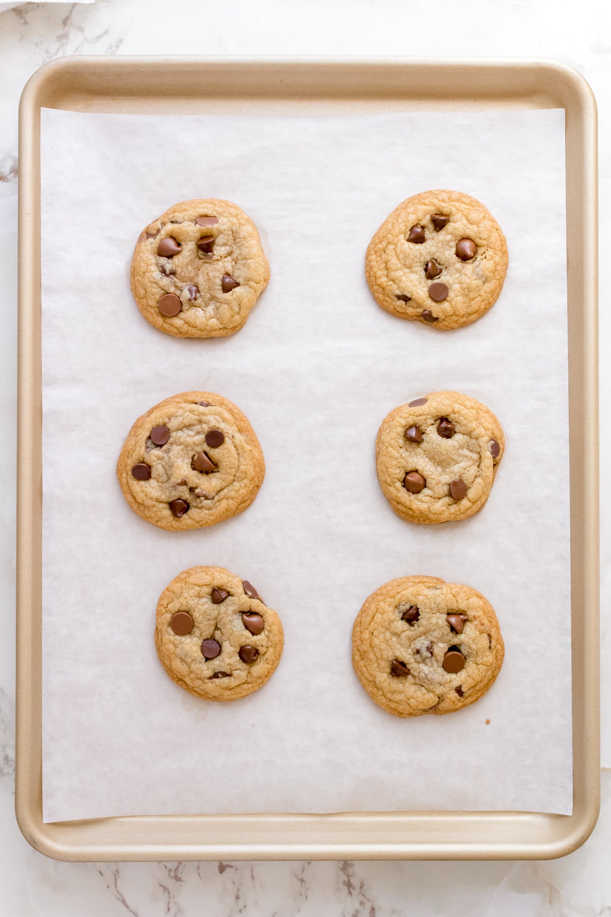 gluten free chocolate chip cookies on parchment lined gold sheet pan.