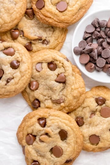 gluten free chocolate chip cookies on white counter with a white bowl of chocolate chips.