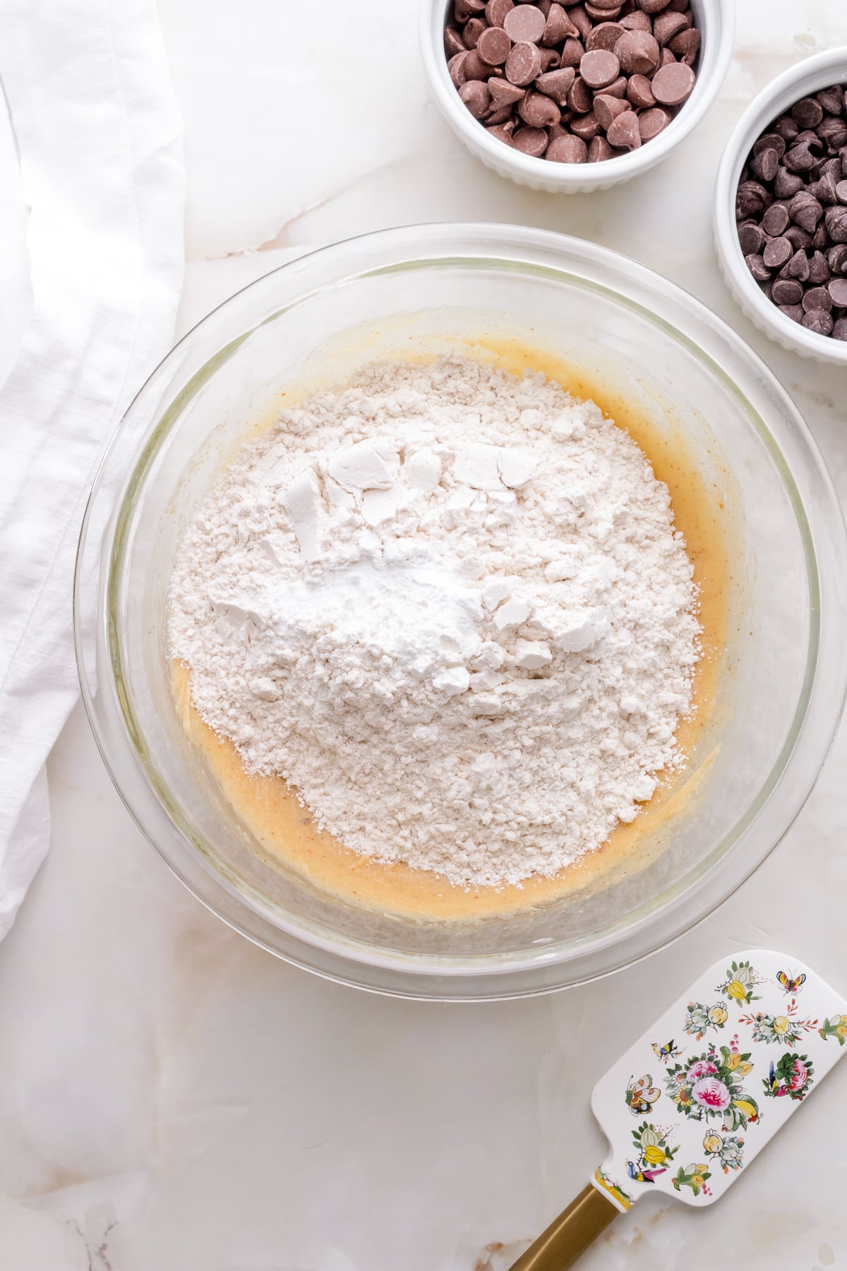 adding dry ingredients to gluten free chocolate chip cookie recipe with spatula and bowl of chocolate chips.