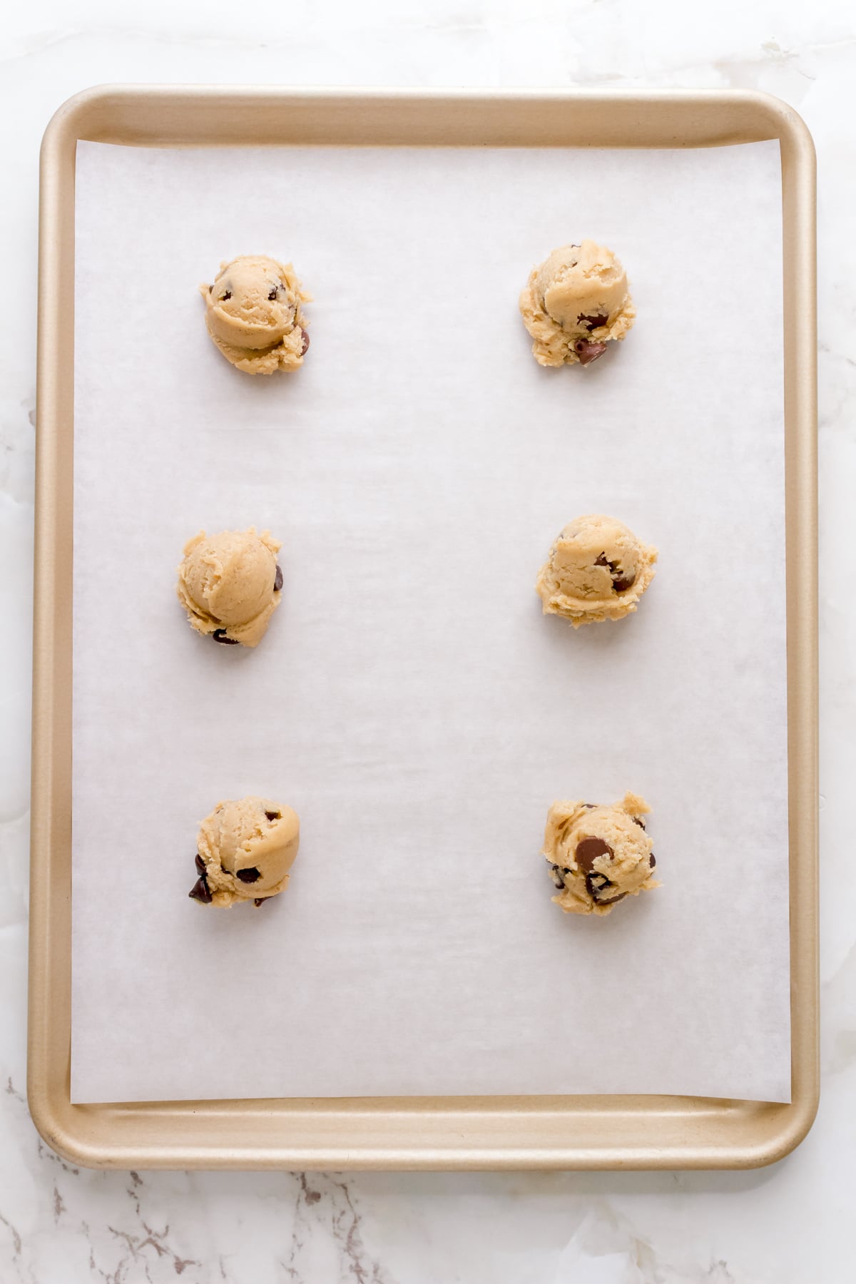 scoops of gluten free chocolate chip cookie dough on parchment lined gold sheet pan.