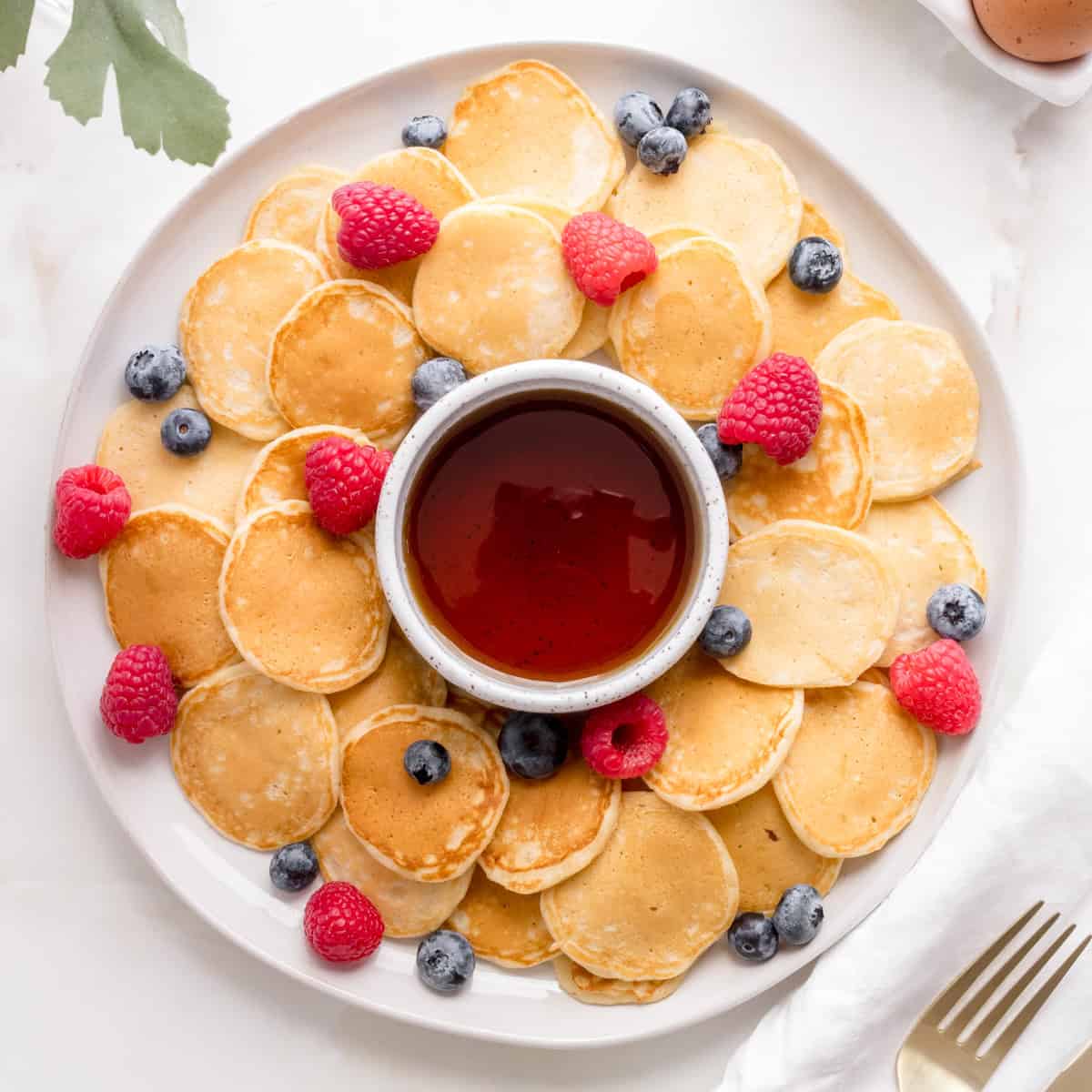 round platter of mini pancakes with berries and maple syrup.