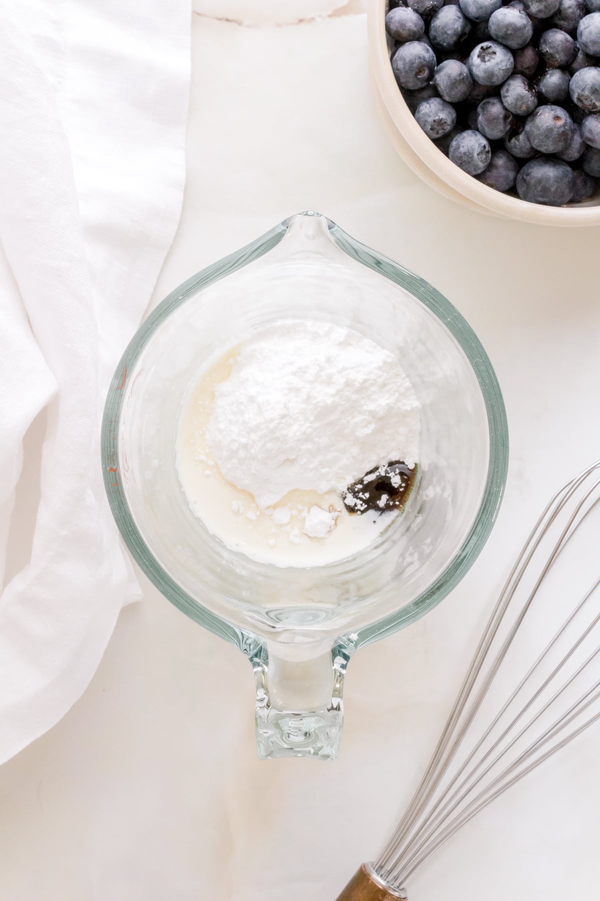 ingredients for vanilla bean glaze in glass measuring cup with a whisk.