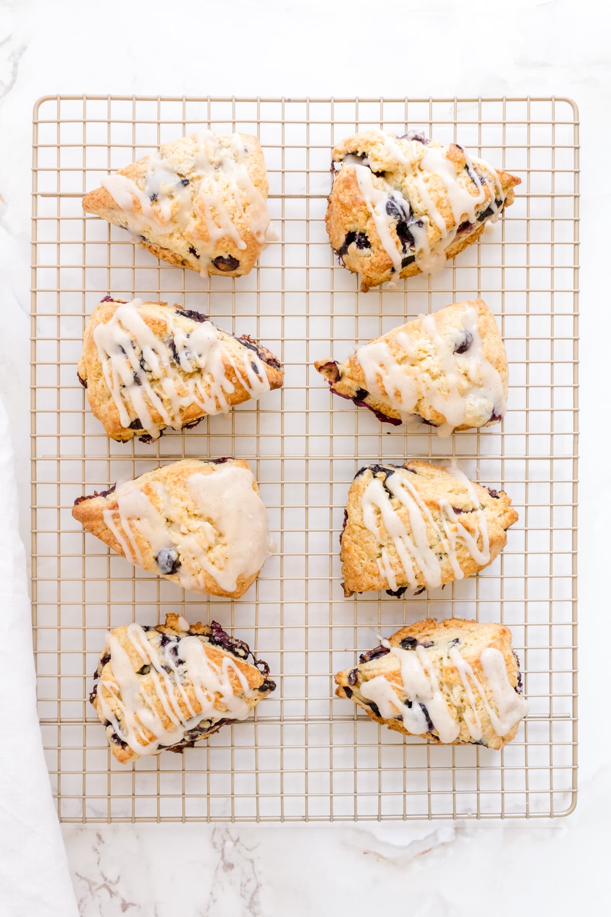 blueberry scones with vanilla bean glaze on copper cooling rack.