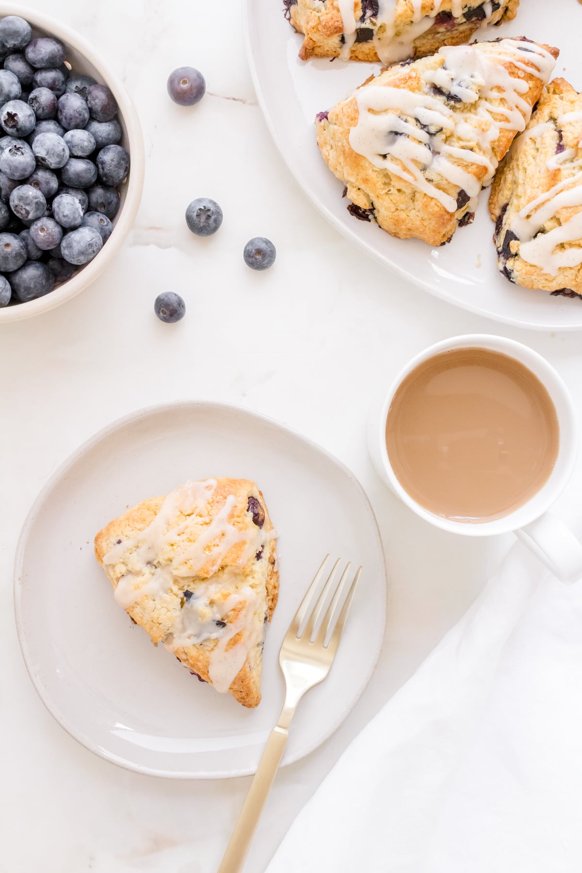 one blueberry scone on a plate with coffee and a bowl of blueberries.