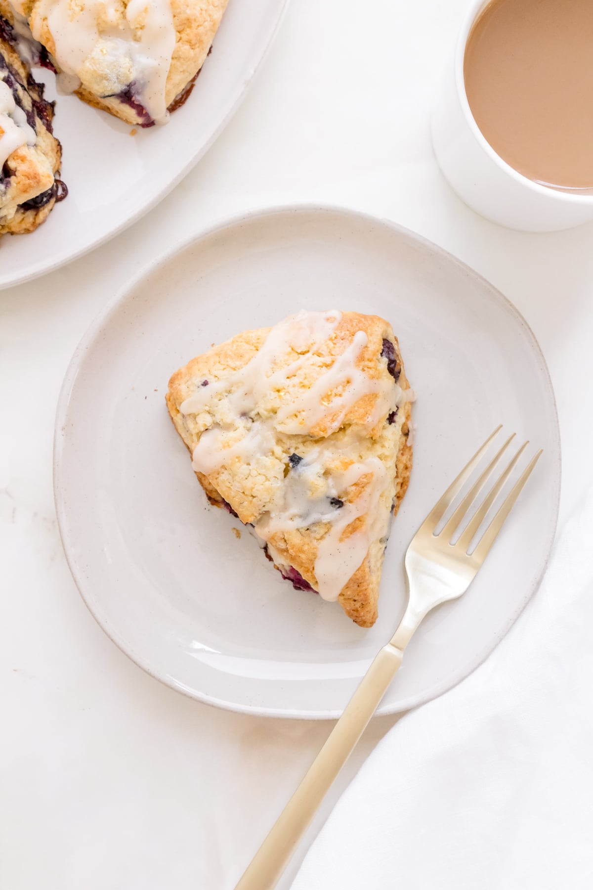 one blueberry scone on plate with gold fork and a mug of coffee.