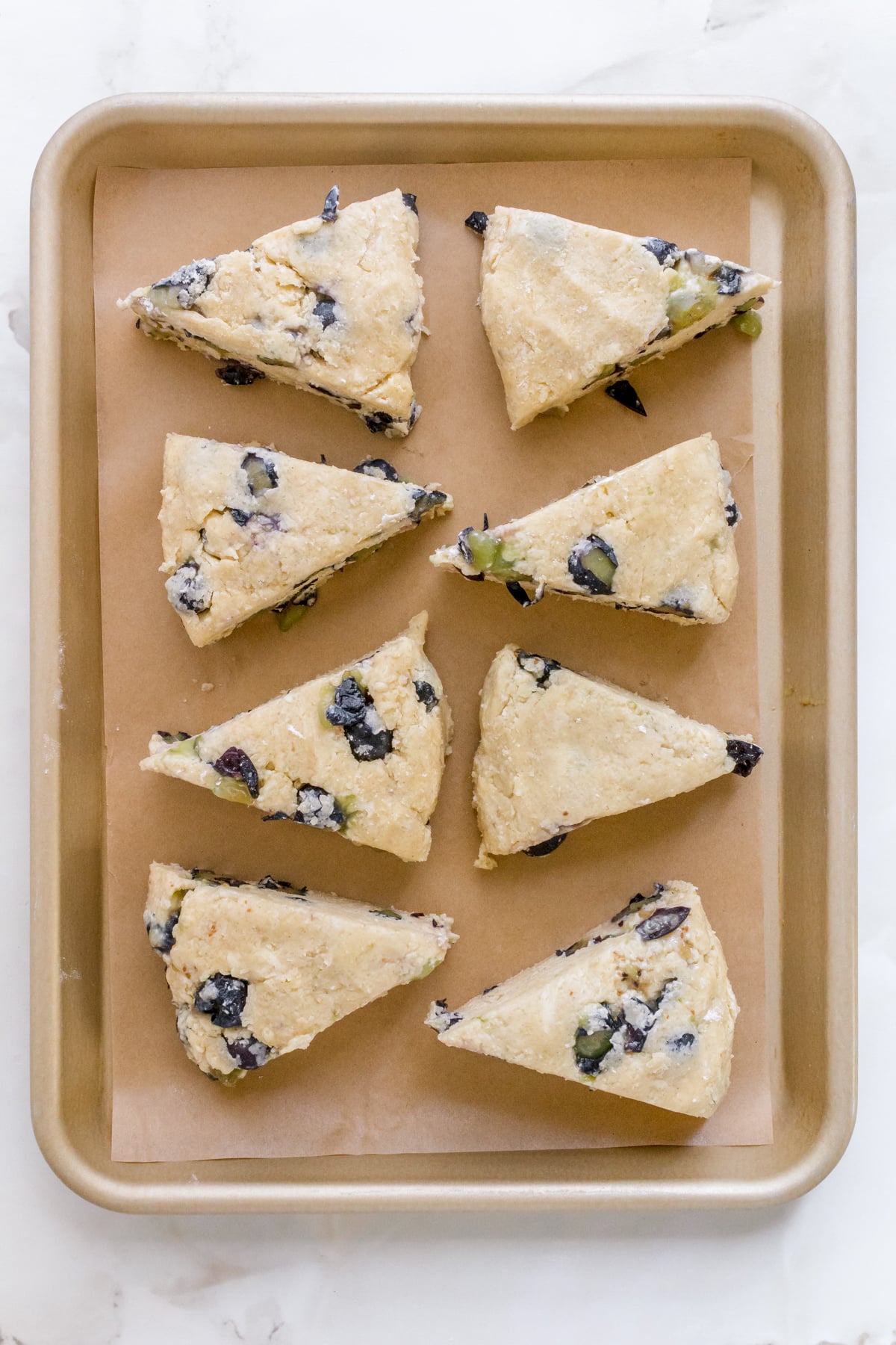 triangles of blueberry scone dough on sheet pan with parchment paper.