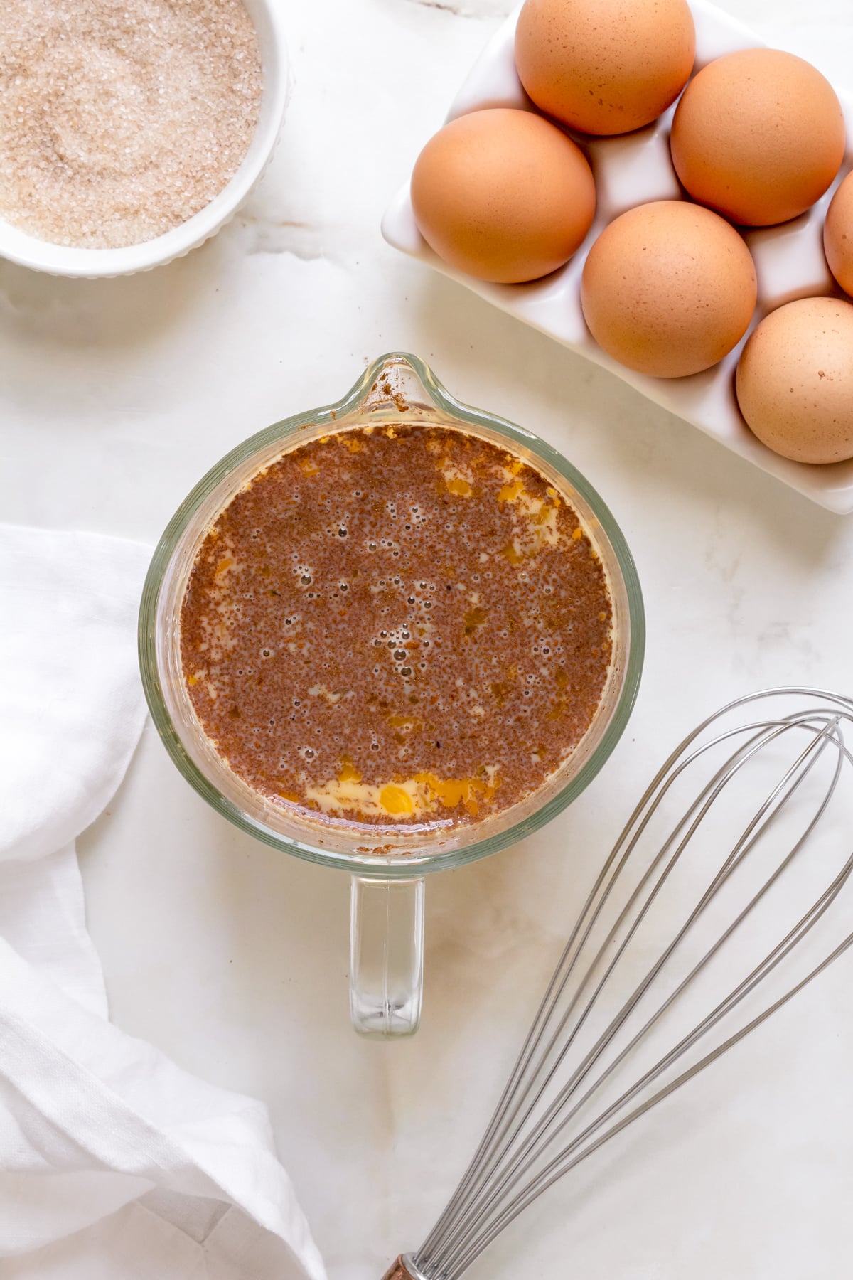 custard for brioche French toast in glass measuring cup with whisk and container of eggs.