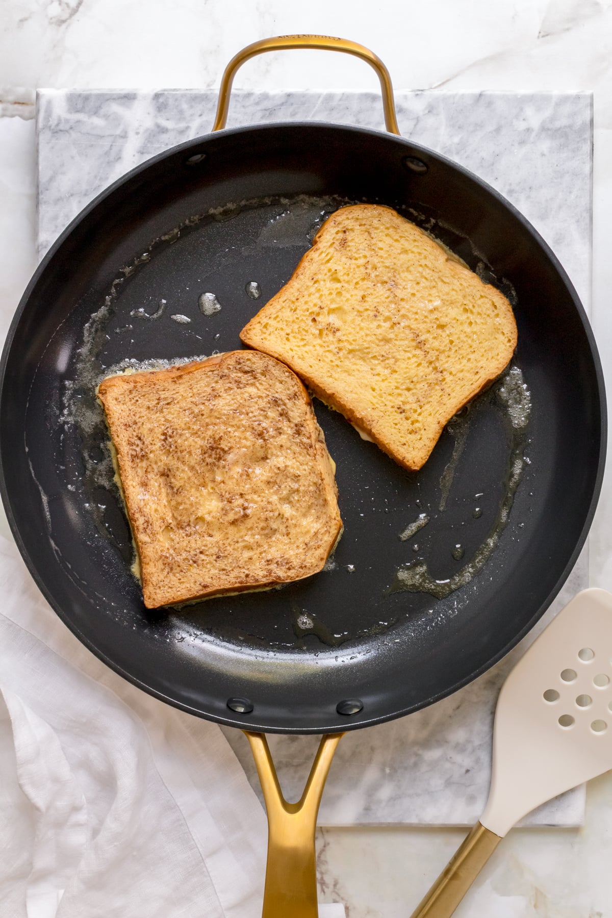 two slices of brioche French toast in frying pan with butter. 