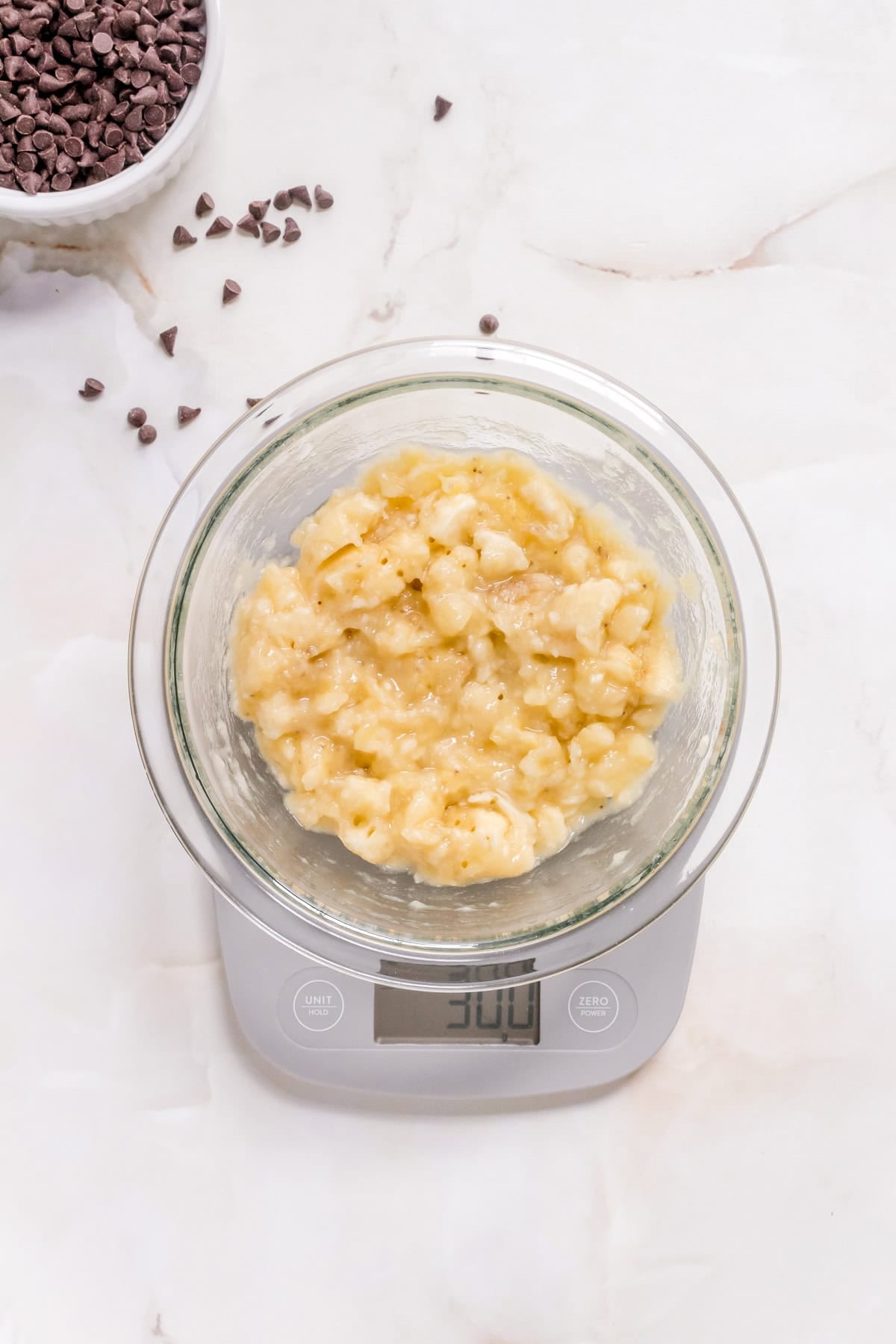 glass bowl of mashed banana on a kitchen scale.