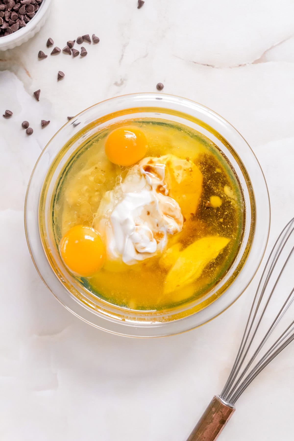 Mashed bananas, Greek yogurt, brown butter, and eggs whisked together in a glass bowl.
