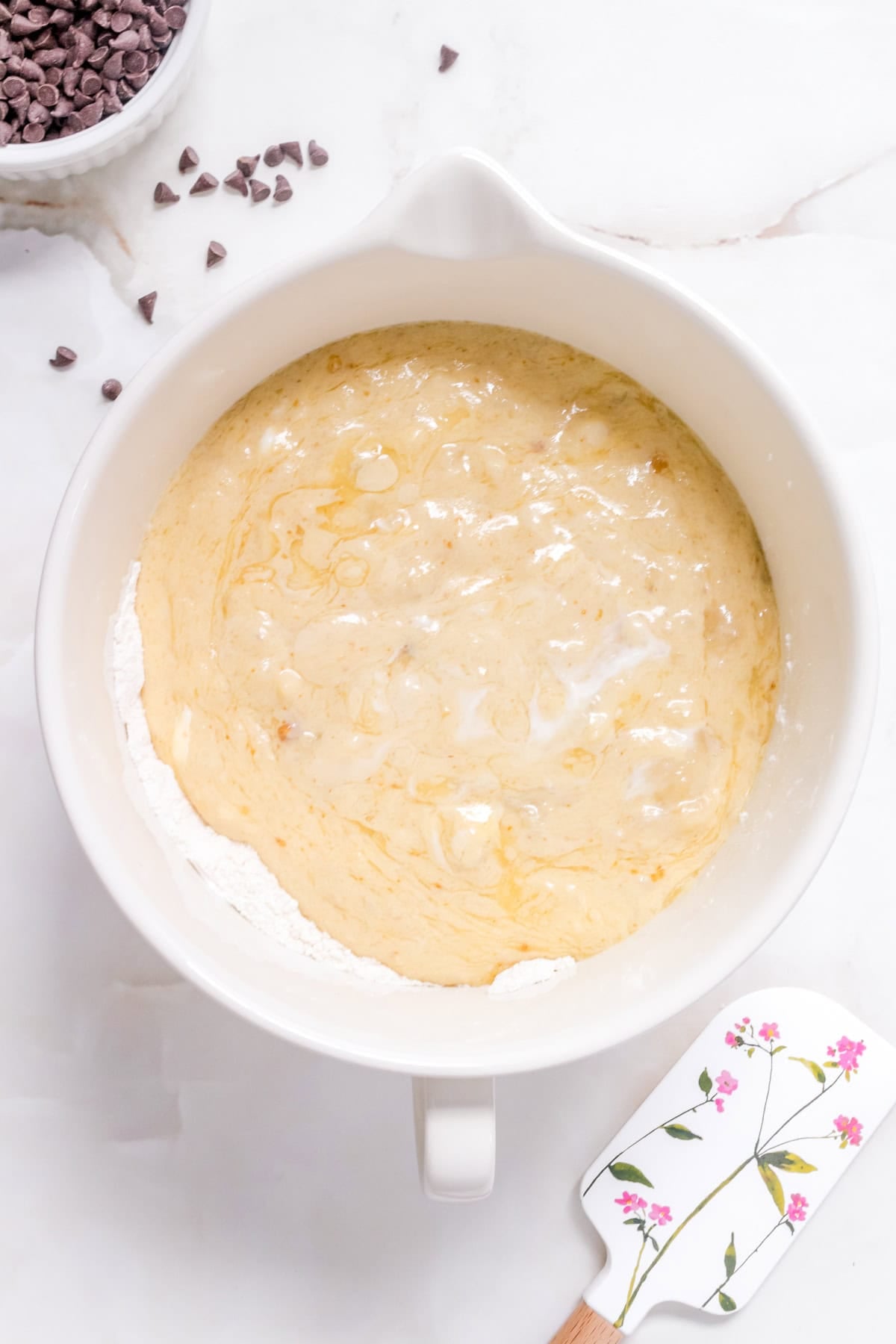 Banana muffin batter being folded together in a white mixing bowl.