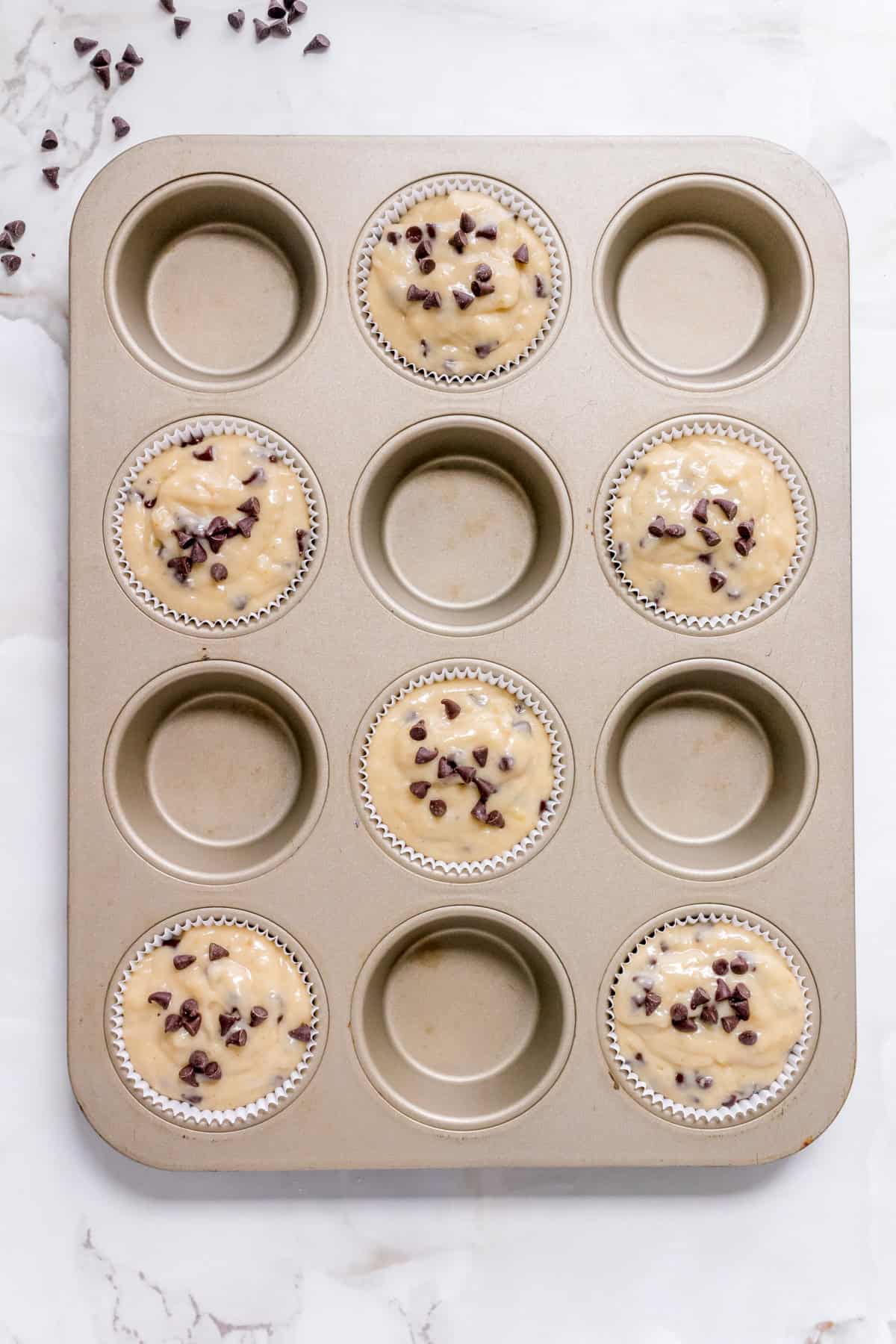 Banana muffin batter scooped into every other cup of a lined muffin pan.