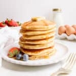 a stack of discard pancakes with a bowl of strawberries and a gold fork.
