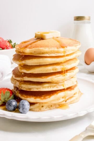 a stack of discard pancakes with a bowl of strawberries and a gold fork.