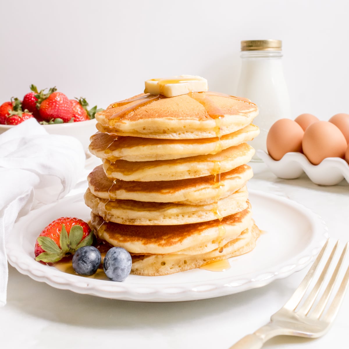 a stack of discard pancakes with a bowl of strawberries and a gold fork.
