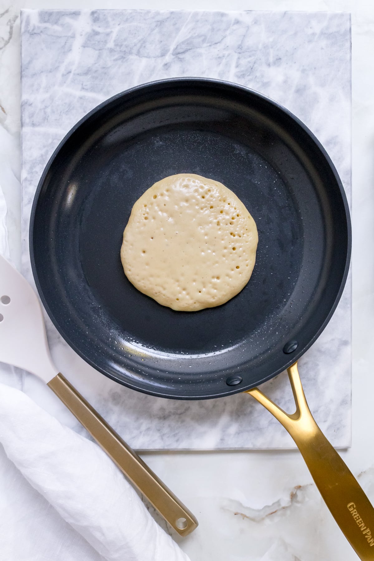discard pancake batter in a frying pan with a spatula on white marble.