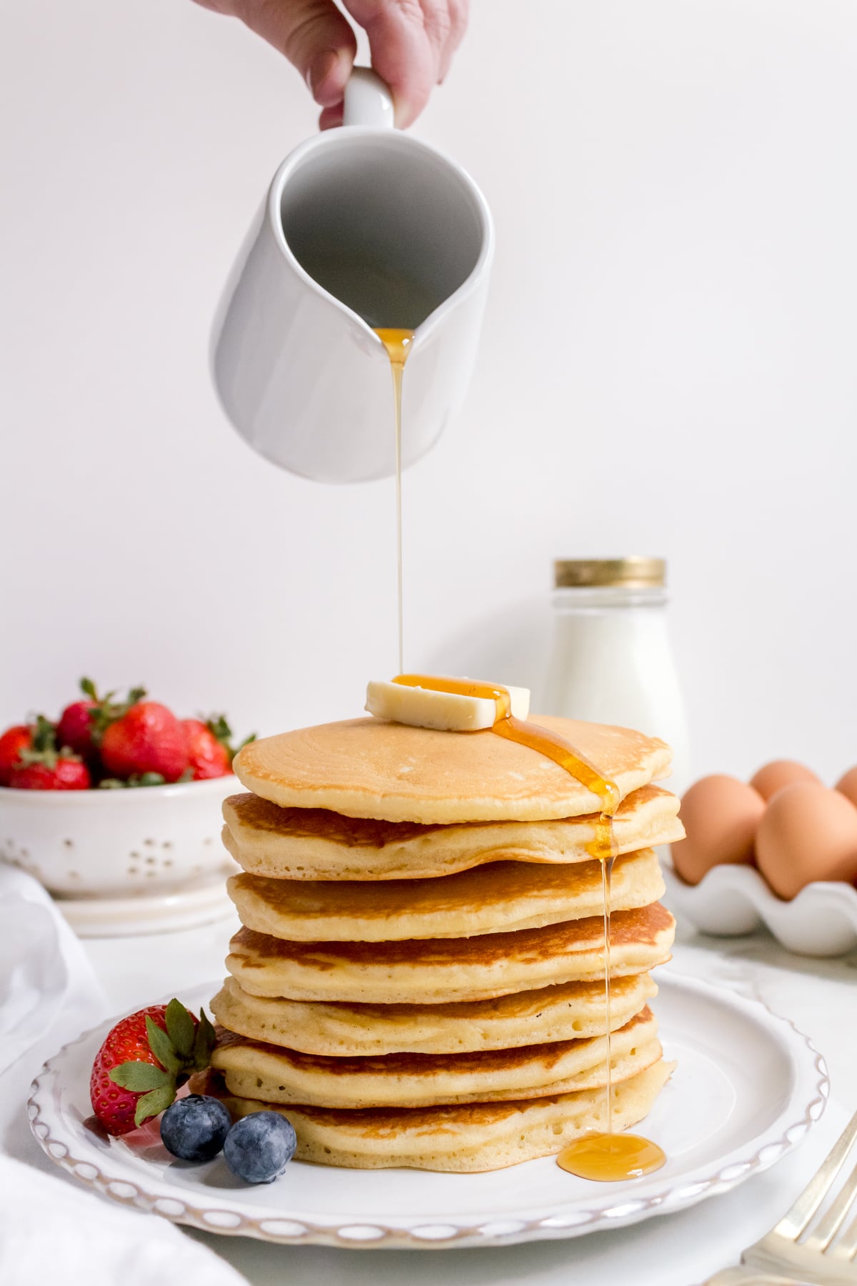 a stack of warm sourdough discard pancakes on white plate with strawberries and eggs. 