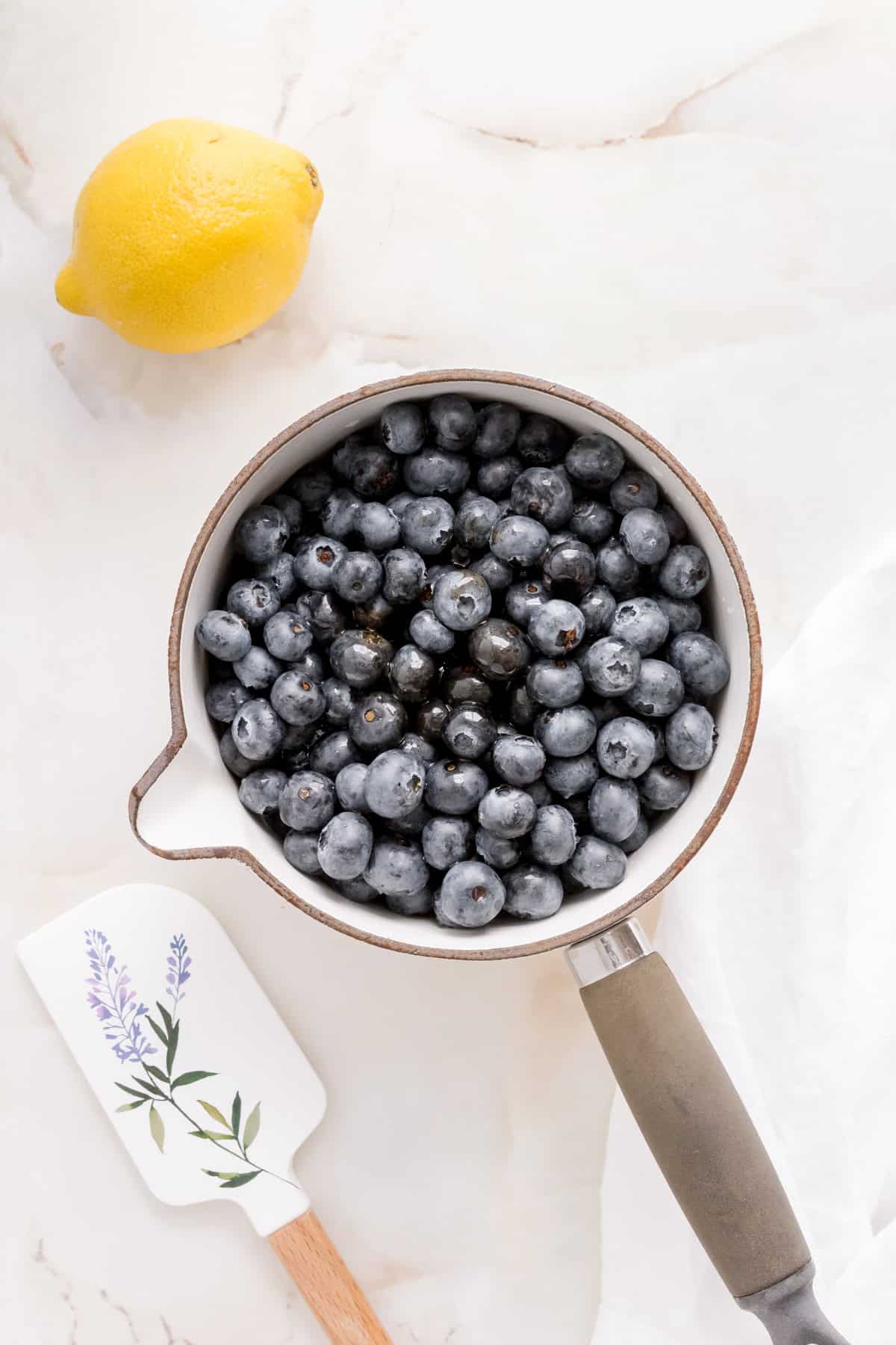 a white saucepan filled with fresh blueberries, maple syrup and vanilla bean paste.