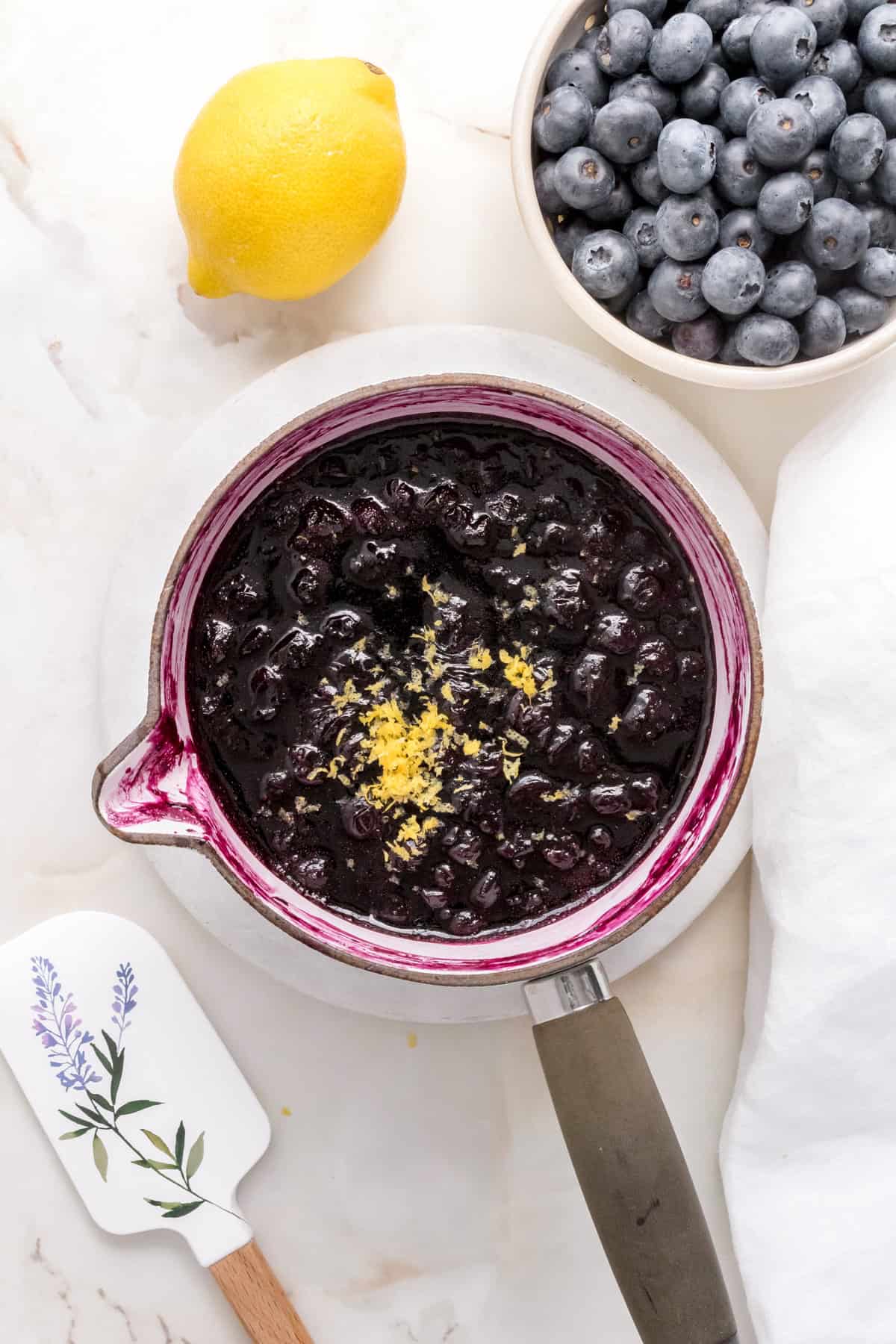 white sauce pan filled fresh blueberry compote with a bowl of blueberries.