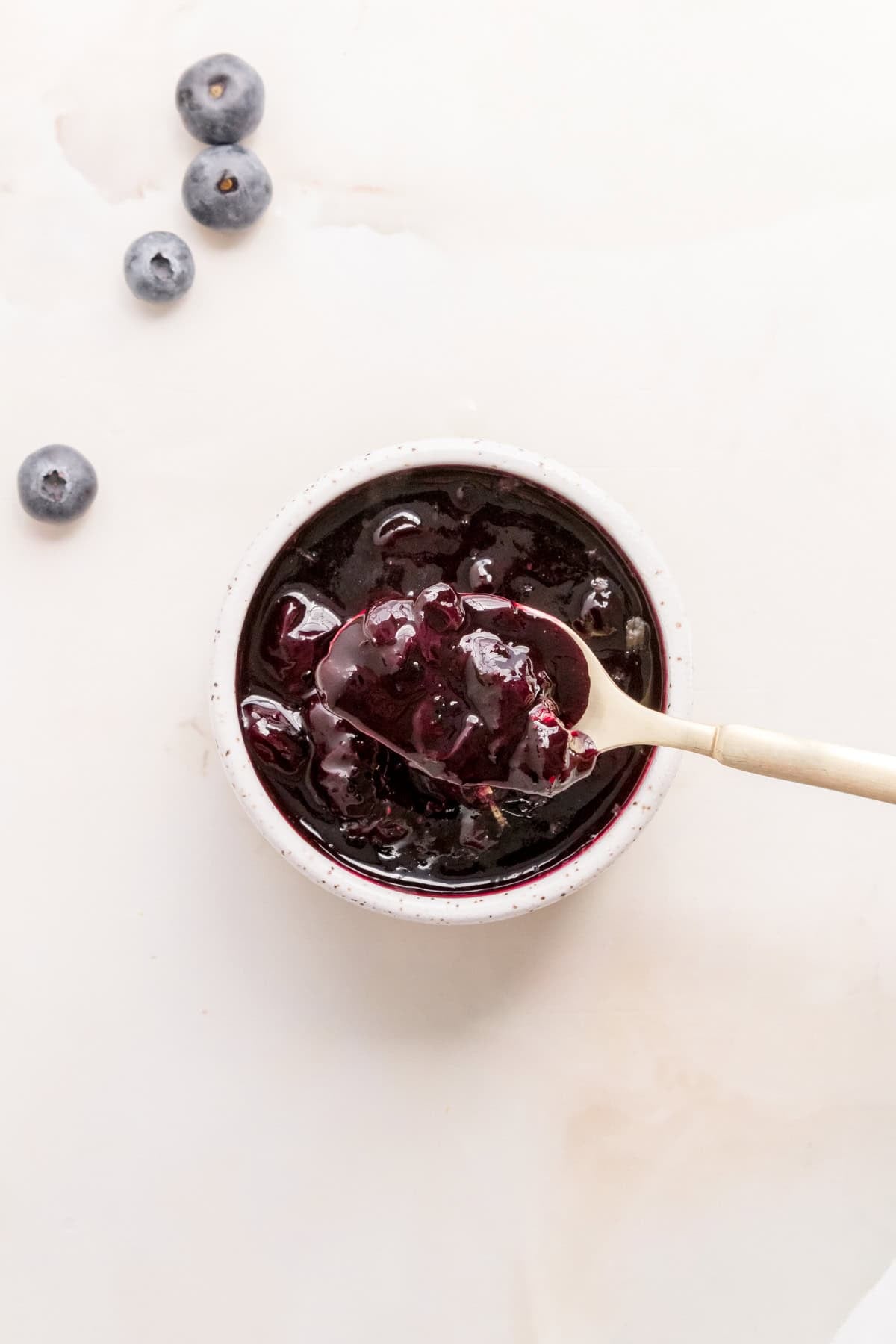a glass jar of blueberry compote with a gold spoon.