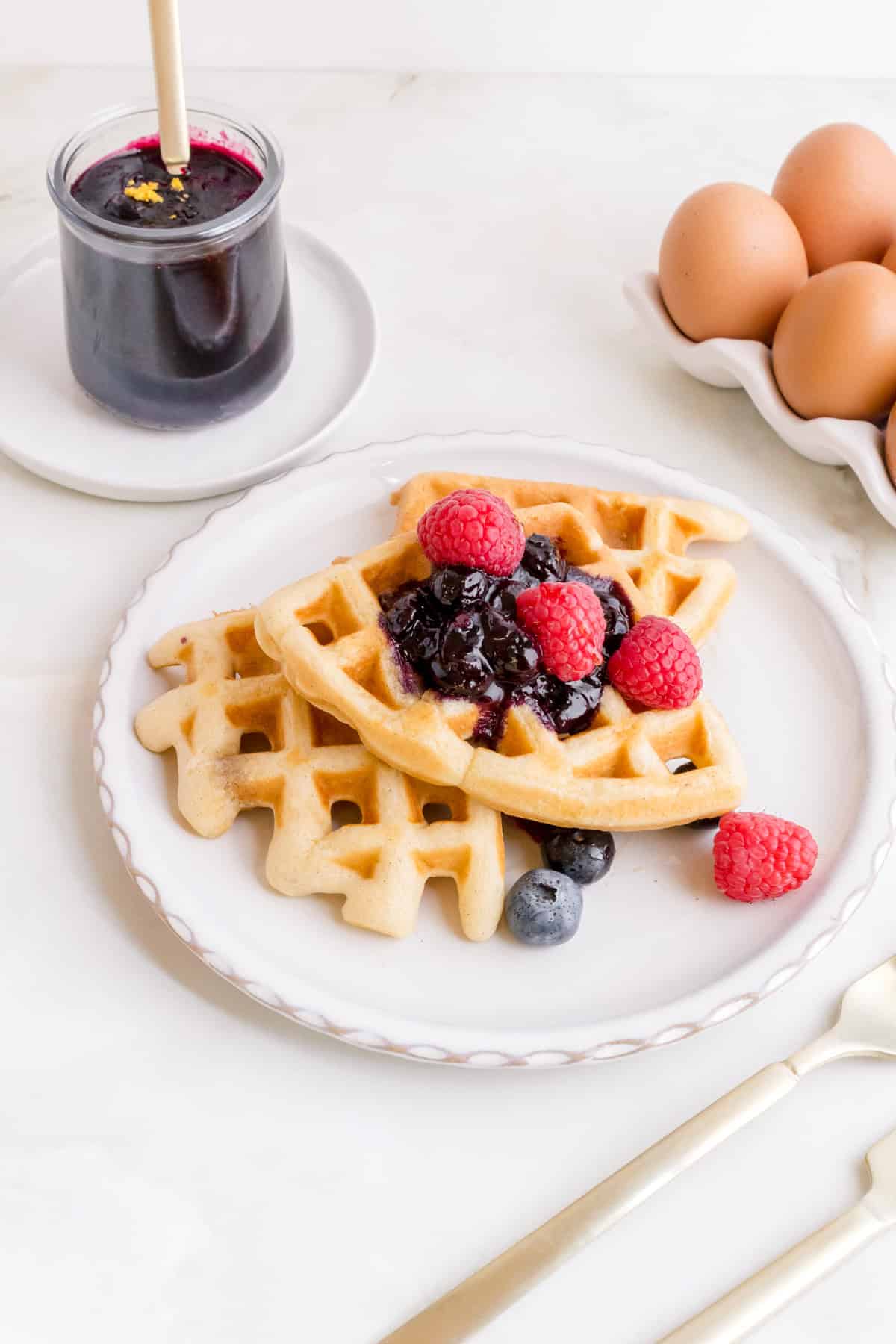 blueberry compote on stack of waffles with a jar of compote in the background.