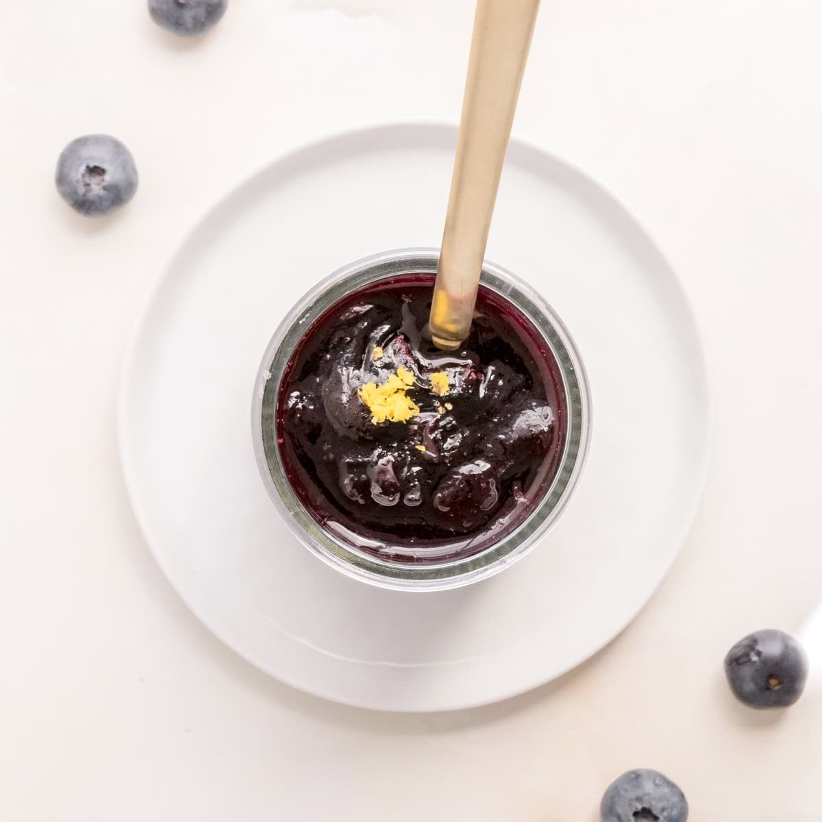 jar of blueberry compote with gold spoon on white counter.