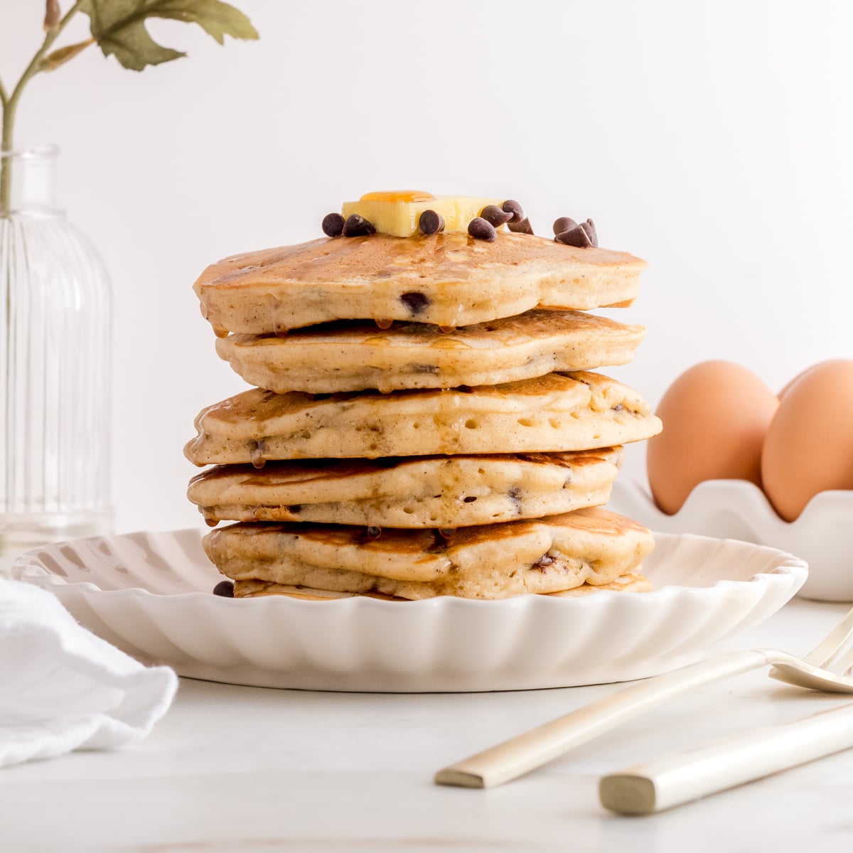 stack of chocolate chip pancakes on white plate with butter and maple syrup.
