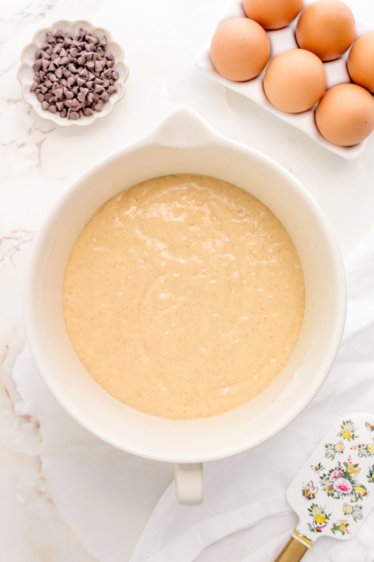 chocolate chip pancake batter in white mixing bowl with spatula.
