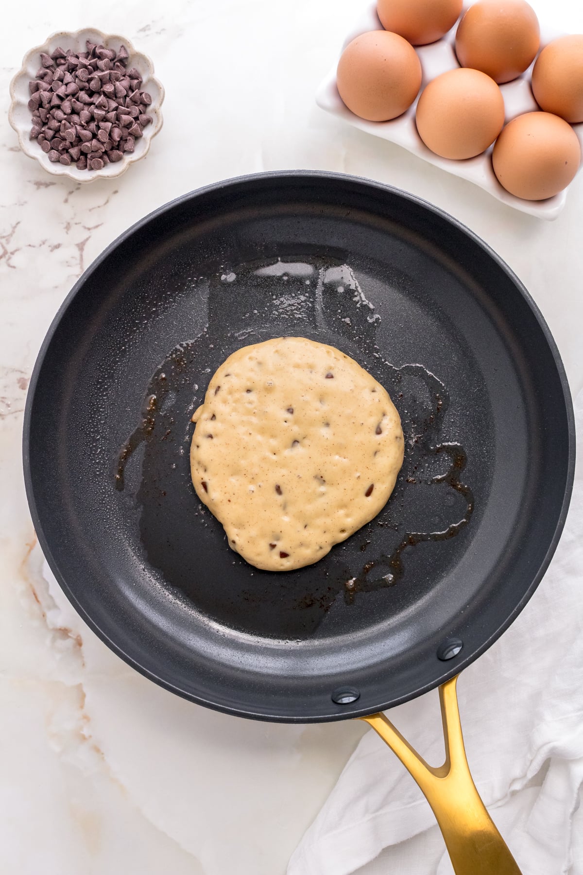 chocolate chip pancake batter cooking in gold frying pan.