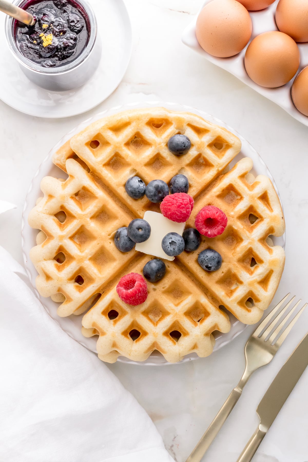 discard waffles with fresh berries on white plate with jar of blueberry compote in background.