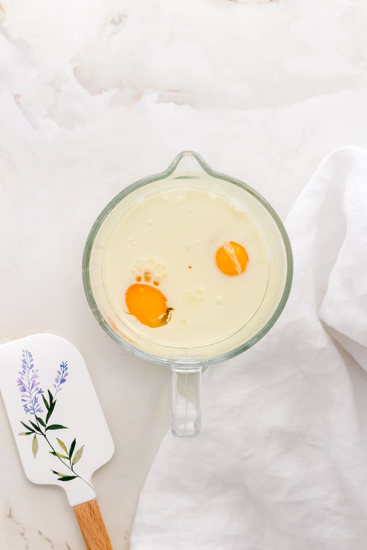 milk, eggs, oil, and vanilla bean paste in glass measuring cup with spatula.