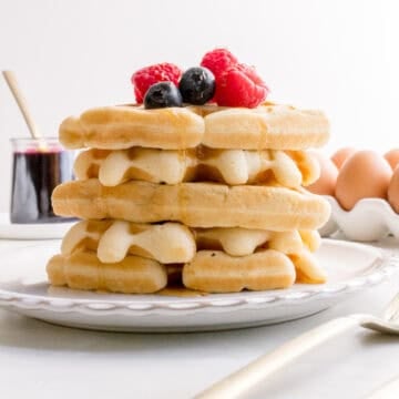 a stack of sourdough discard waffles on a white plate with fresh berries and maple syrup.