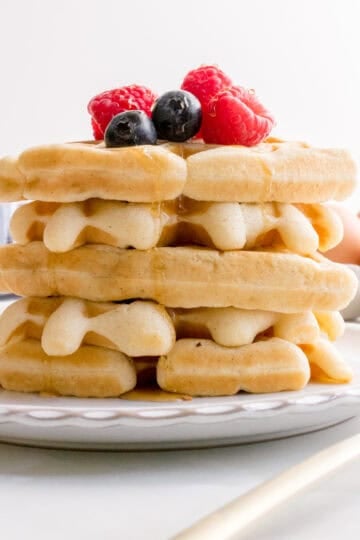 a stack of sourdough discard waffles on a white plate with fresh berries and maple syrup.