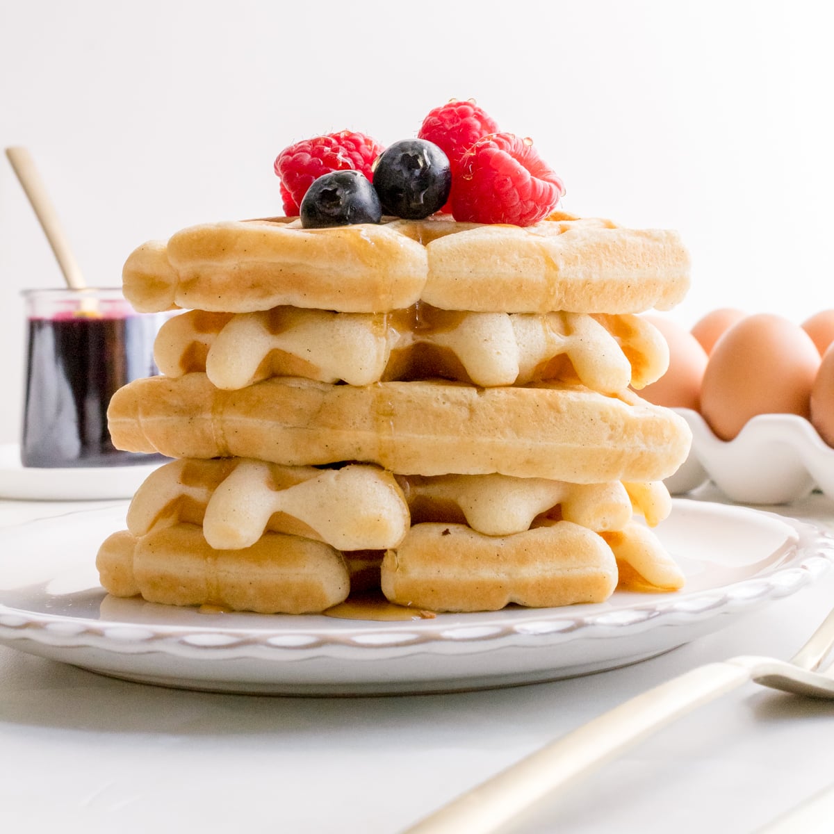 a stack of sourdough discard waffles on a white plate with fresh berries and maple syrup.