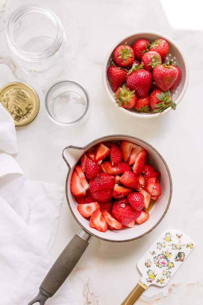 ingredients for strawberry compote in white saucepan with spatula.