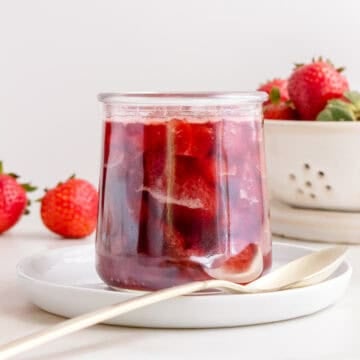 glass of of strawberry compote with a gold spoon and a dish of strawberries.