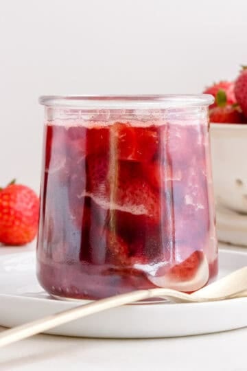 glass of of strawberry compote with a gold spoon and a dish of strawberries.