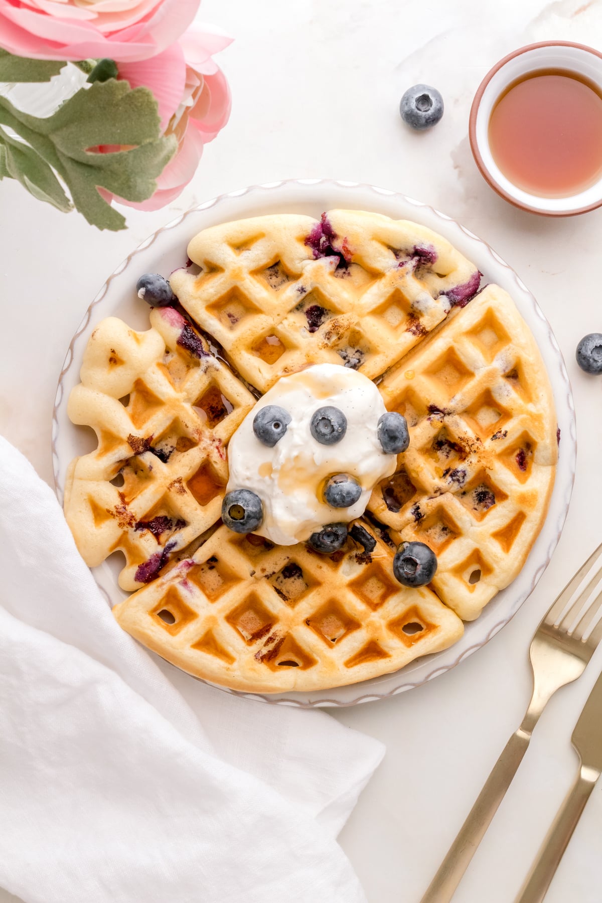 blueberry waffles on white plate with whipped cream and maple syrup.