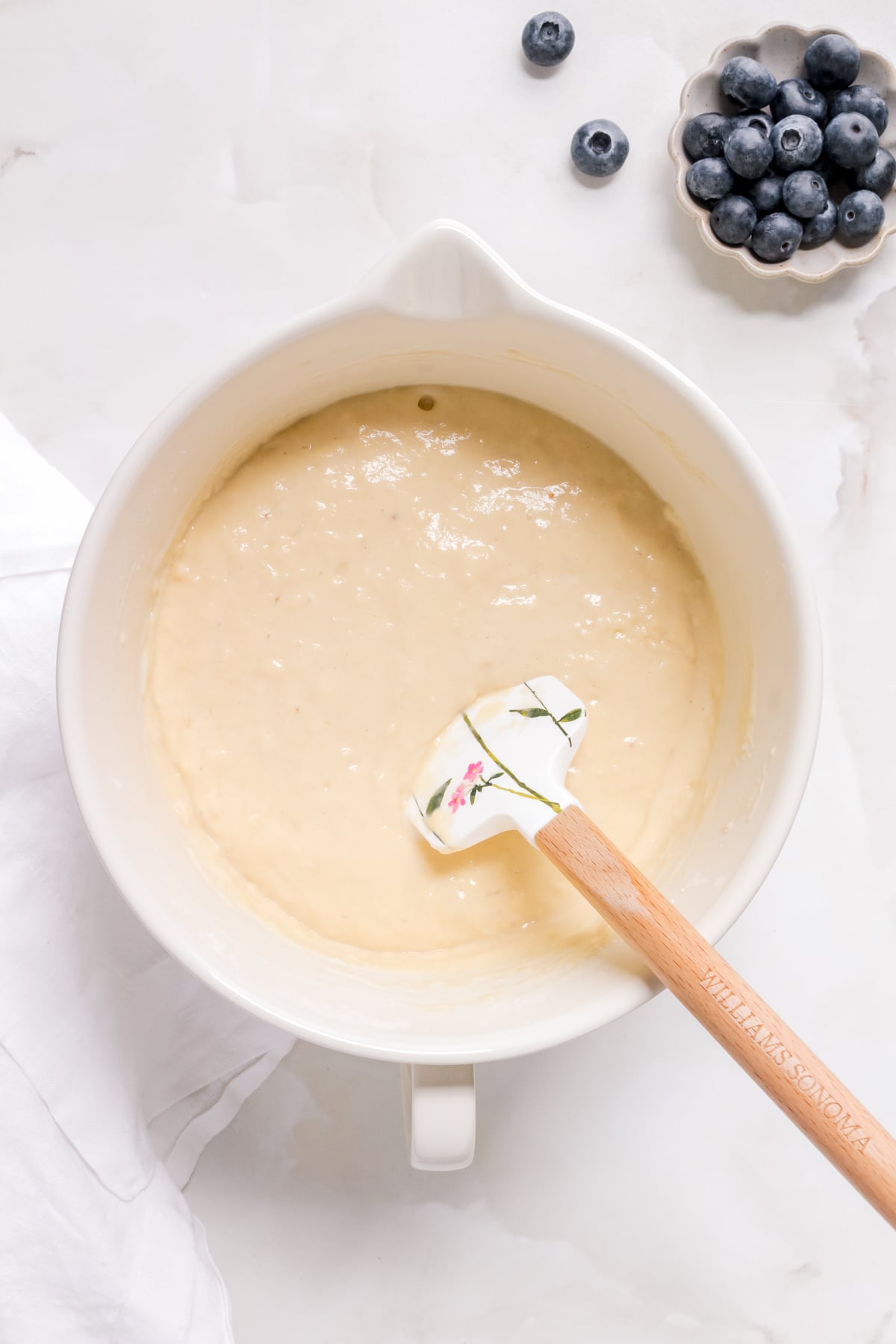 white bowl of waffle batter with spatula and a small bowl of blueberries.