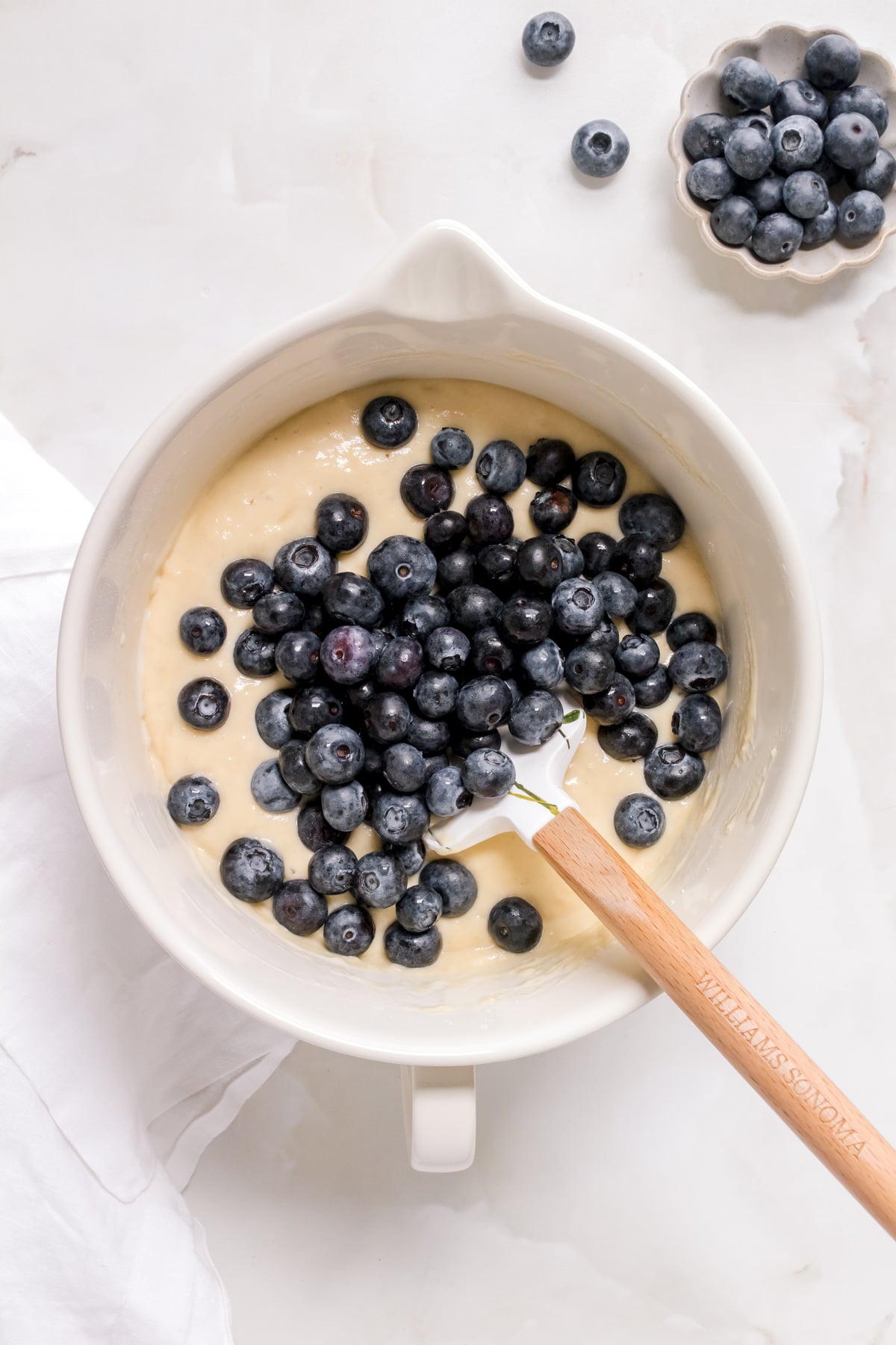adding blueberries to waffle batter in ceramic mixing bowl with spatula.