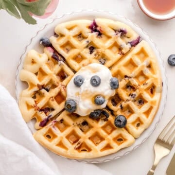 blueberry waffles with whipped cream on white plate with gold fork and knife.
