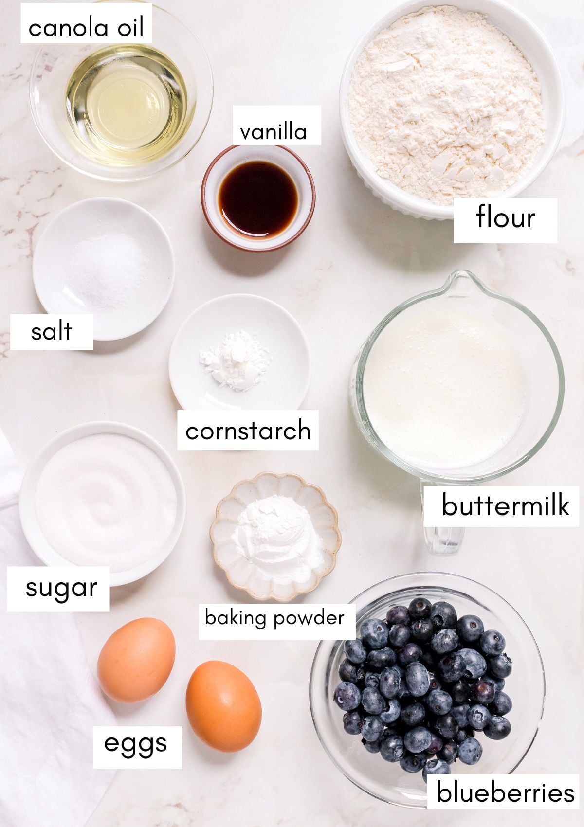 small bowls of labeled ingredients for blueberry waffles on pink marble counter.