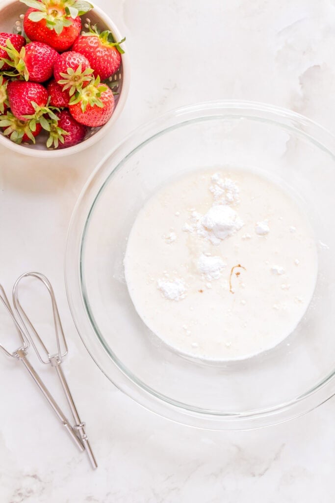 heavy cream, vanilla bean paste, and confectioners' sugar in large mixing bowl on marble counter.