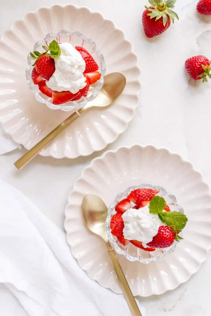 dishes strawberries with whipped cream with gold spoons on marble counter.