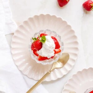 homemade whipped cream with strawberries in glass dish with a gold spoon.
