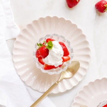 homemade whipped cream with strawberries in glass dish with a gold spoon.