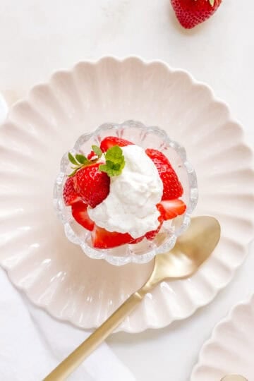 homemade whipped cream with strawberries in glass dish with a gold spoon.